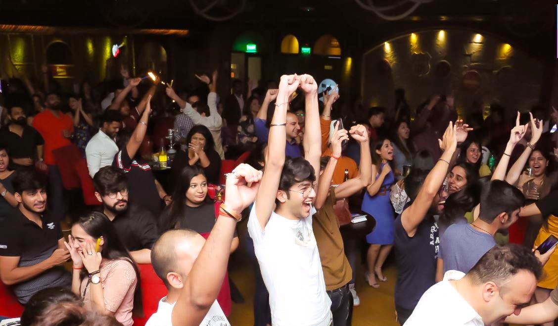 Crowd celebrating with raised arms at a warmly lit Delhi event