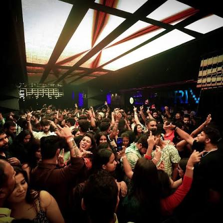 Dense Delhi crowd dancing under patterned club lighting