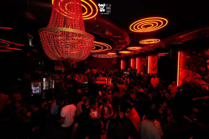 Crowded Mumbai club lit in red with a statement chandelier overhead