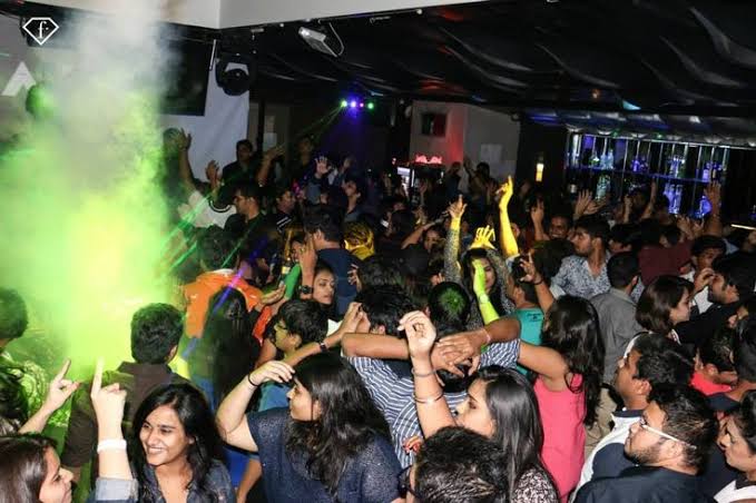 Crowd raising hands under green and blue smoke at a Pune techno night